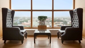Ein Zimmer mit zwei Ledersesseln und einem kleinen Tisch, ein großes Fenster mit Blick auf die Stadt und ein Blumentopf auf dem Fensterbrett.
