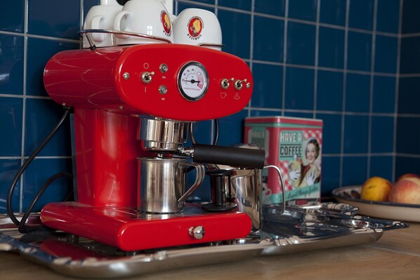 Une machine à expresso rouge, dotée d’un manomètre et surmontée de deux tasses blanches.