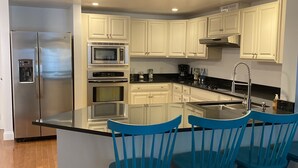 A modern kitchen with white cabinets, stainless steel appliances, and a central island with blue chairs. - Crashing surf, steps to the sand, Pier BEST CONDO IN OLD ORCHARD BEACH (Old Orchard Beach)