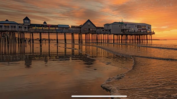 A waterfront property with multiple buildings on stilts, a restaurant, and a view of the ocean at sunset. - Crashing surf, steps to the sand, Pier BEST CONDO IN OLD ORCHARD BEACH (Old Orchard Beach)