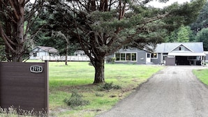 A gravel driveway leading to a house with a garage, surrounded by trees and a grassy field.