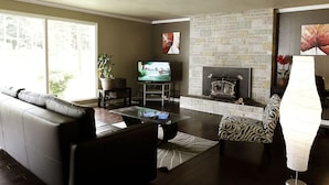 A living room with a sofa, a glass coffee table, a television, a fireplace, and a patterned armchair.