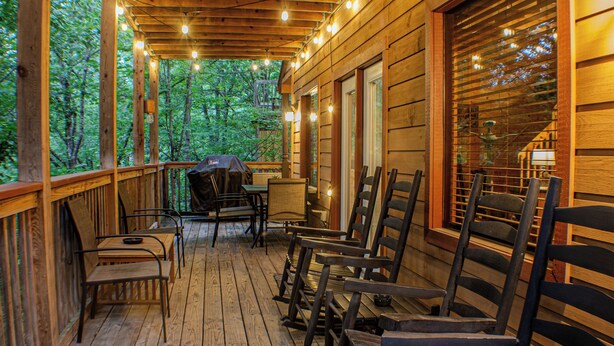 Eine Holzterrasse mit Stühlen und einem Grill, umgeben von Bäumen.