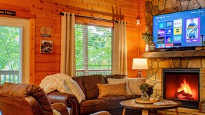 Ein gemütliches Wohnzimmer mit Kamin aus Stein, Holzwänden und einem flachbildfernseher, der darüber angebracht ist.