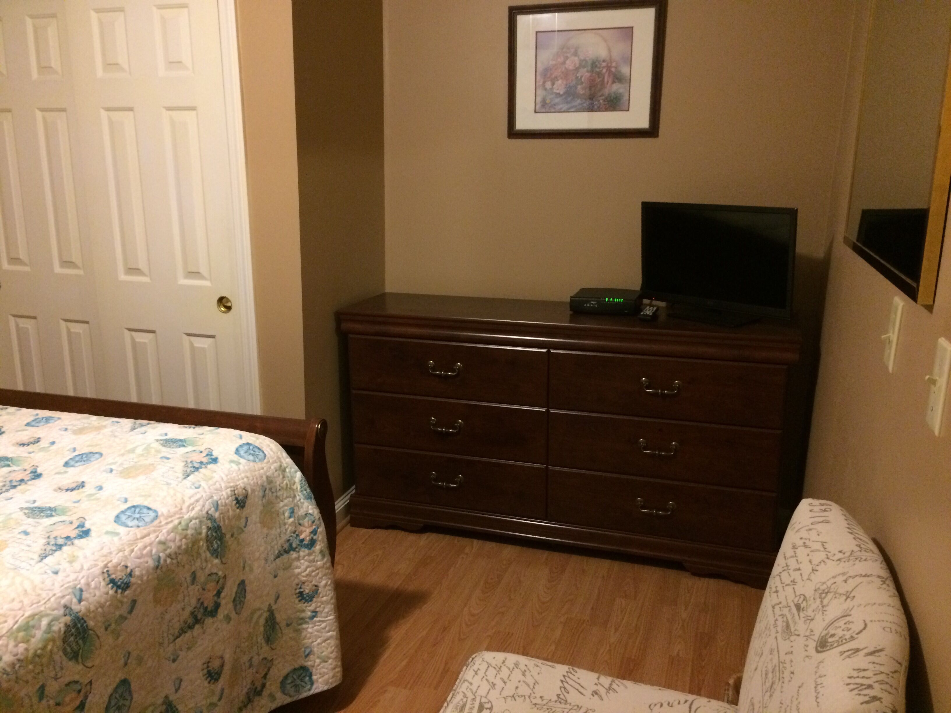 Una habitación con una cama, un tocador, un televisor encima del tocador y un cuadro en la pared.