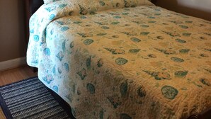 Una cama bien hecha con una colcha y almohadas de estampado floral, un cuadro con flores encima de la cama y una lámpara en la mesita de noche.
