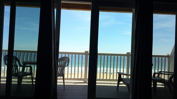 Vista desde una habitación con ventanas amplias a un balcón con vista a la playa.