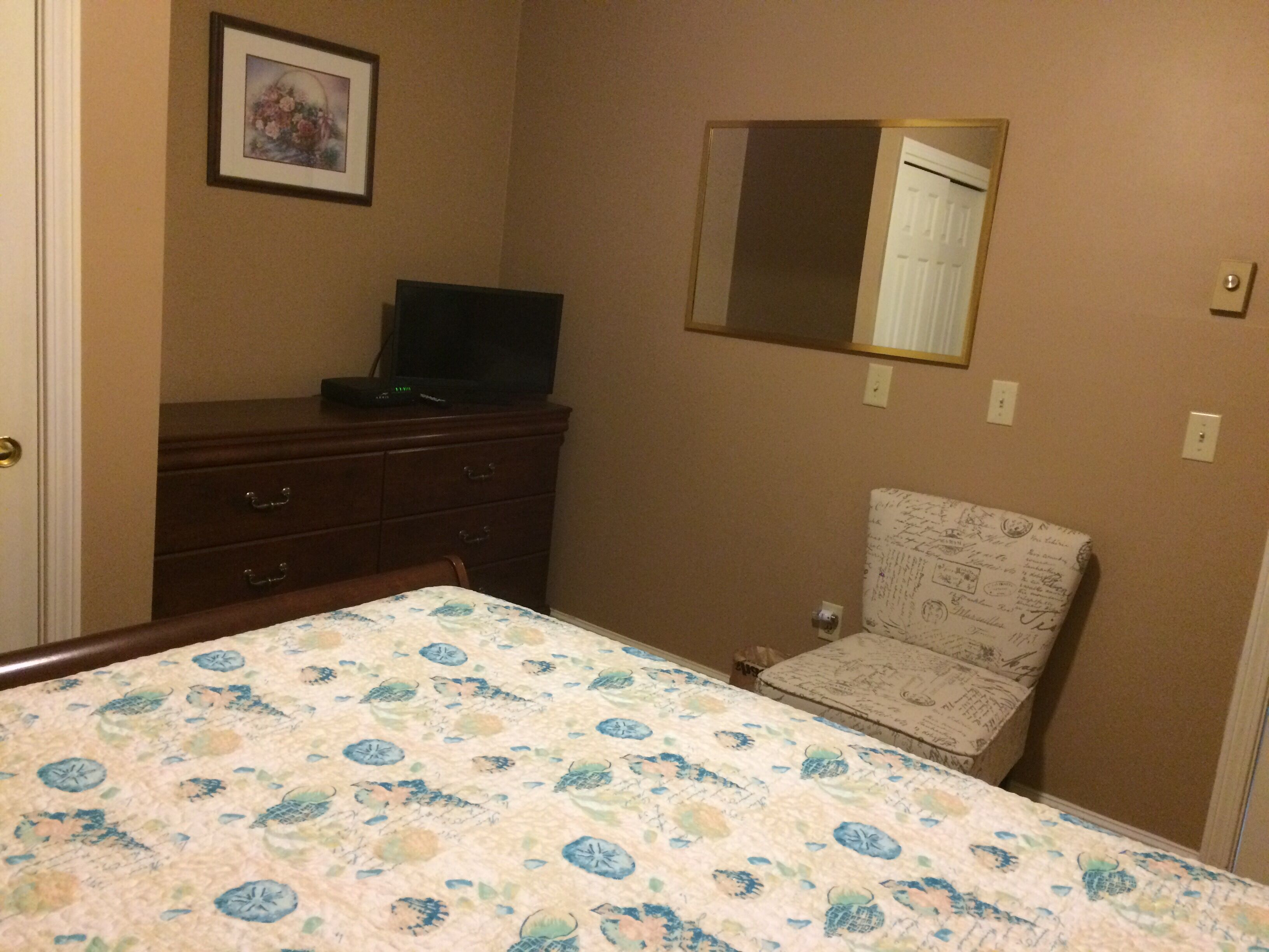 A bedroom with a bed, a dresser, a chair, a television, and a mirror.