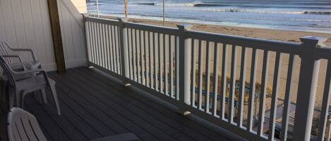 A wooden deck with a white railing overlooking a beach.