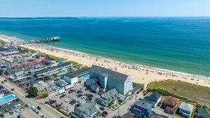 Vista aérea de una zona costera con playa, muelle y una combinación de edificios residenciales y comerciales.