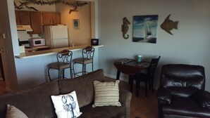 Una sala de estar con un sofá marrón, un sillón de cuero negro y un comedor con una mesa y sillas.
