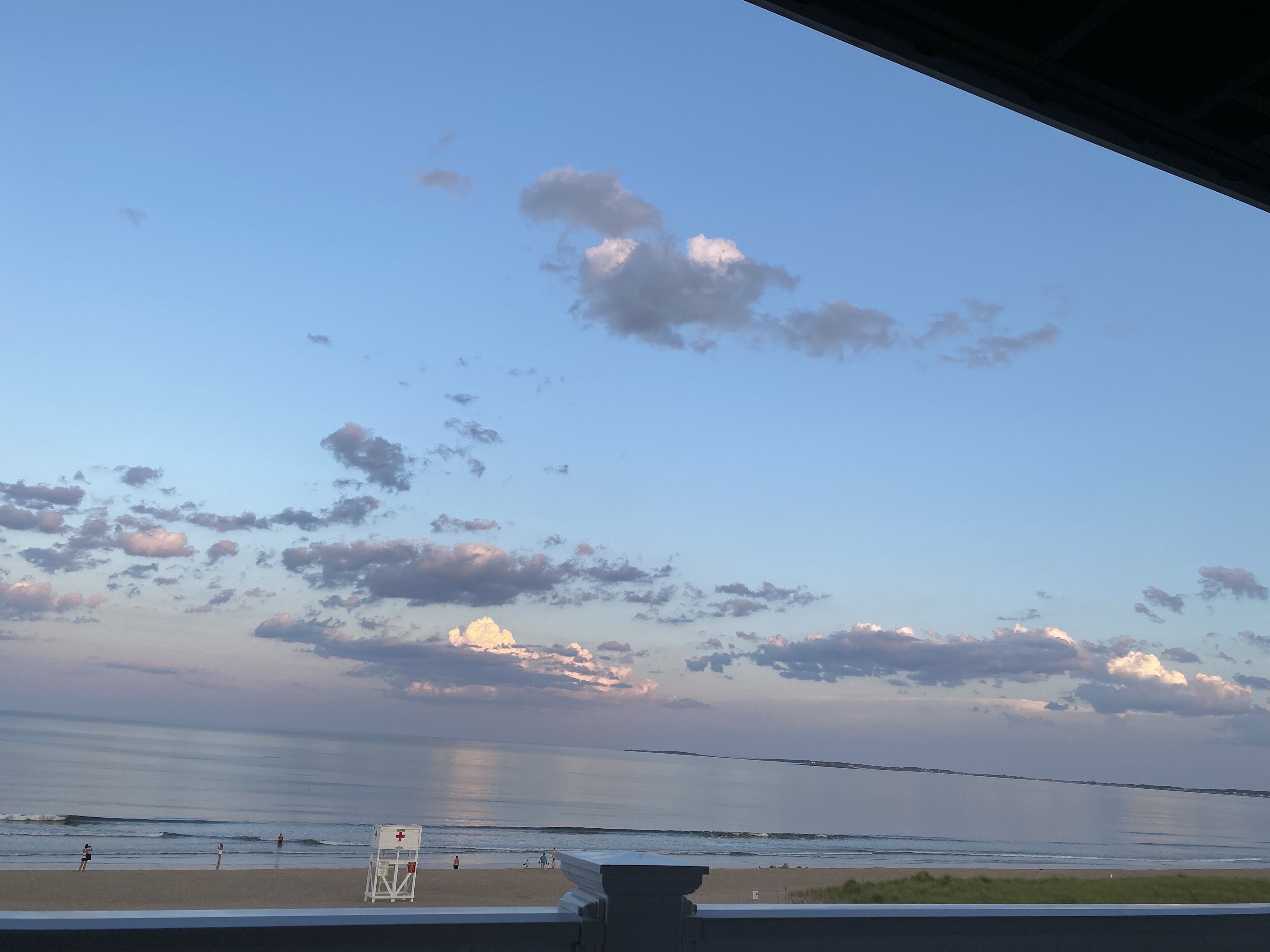 A beach view with a lifeguard tower, calm sea, and a clear sky with scattered clouds.