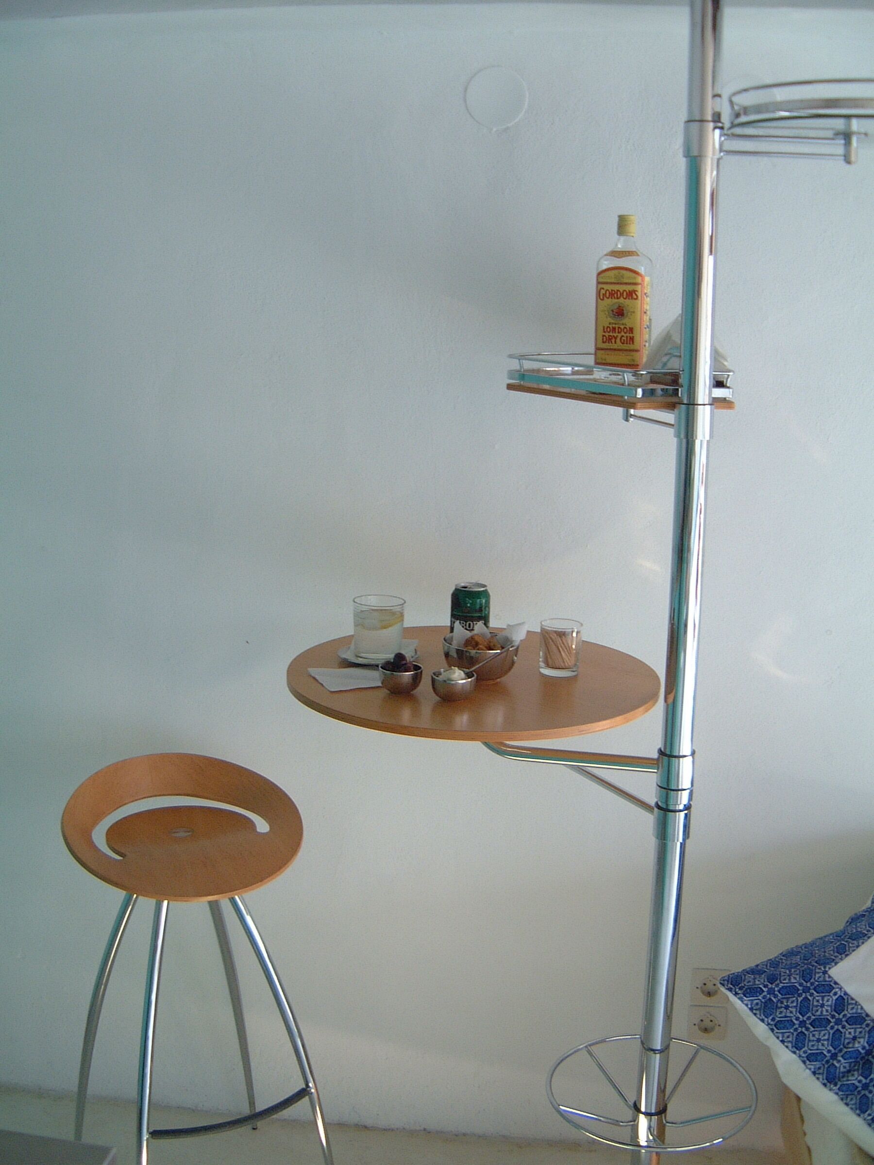 A bathroom with a small round table, a stool, a shelf with toiletries, and a mirror.