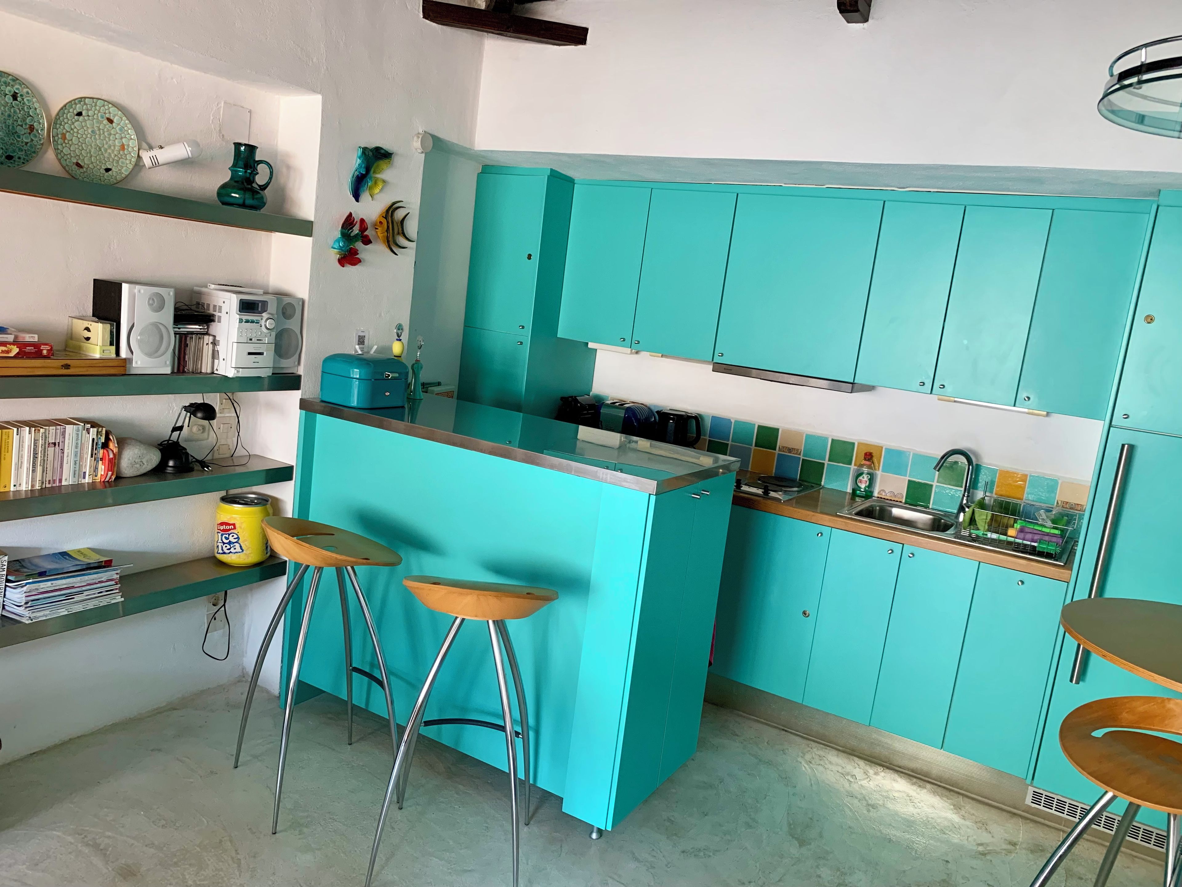 A kitchen with teal cabinets, a central island with stools, and a variety of kitchen appliances.