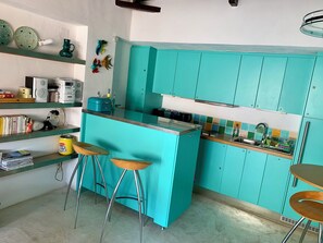 A kitchen with teal cabinets, a central island with stools, and a variety of kitchen appliances.