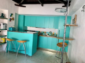 A kitchen with teal cabinets, a central island with stools, and a high ceiling with exposed beams.