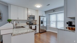 Una cocina moderna con armarios blancos, electrodomésticos de acero inoxidable y suelo de madera.