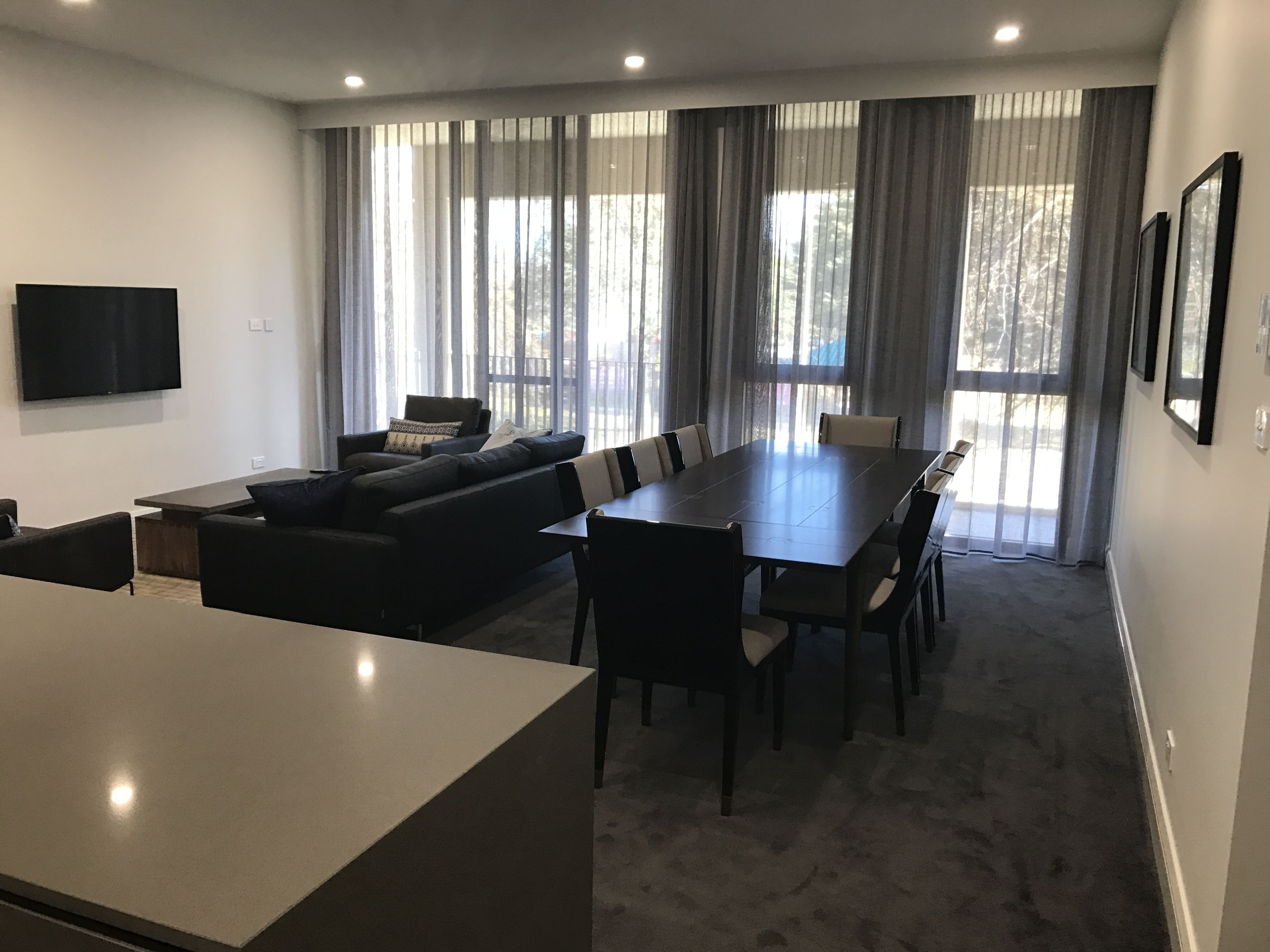Una sala de estar moderna con un sofá seccional, una mesa de comedor y un televisor de pantalla plana montado en la pared.