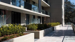 A modern building with multiple balconies, a paved walkway, and landscaped areas with shrubs. - Knightsbridge Canberra (Kingston)