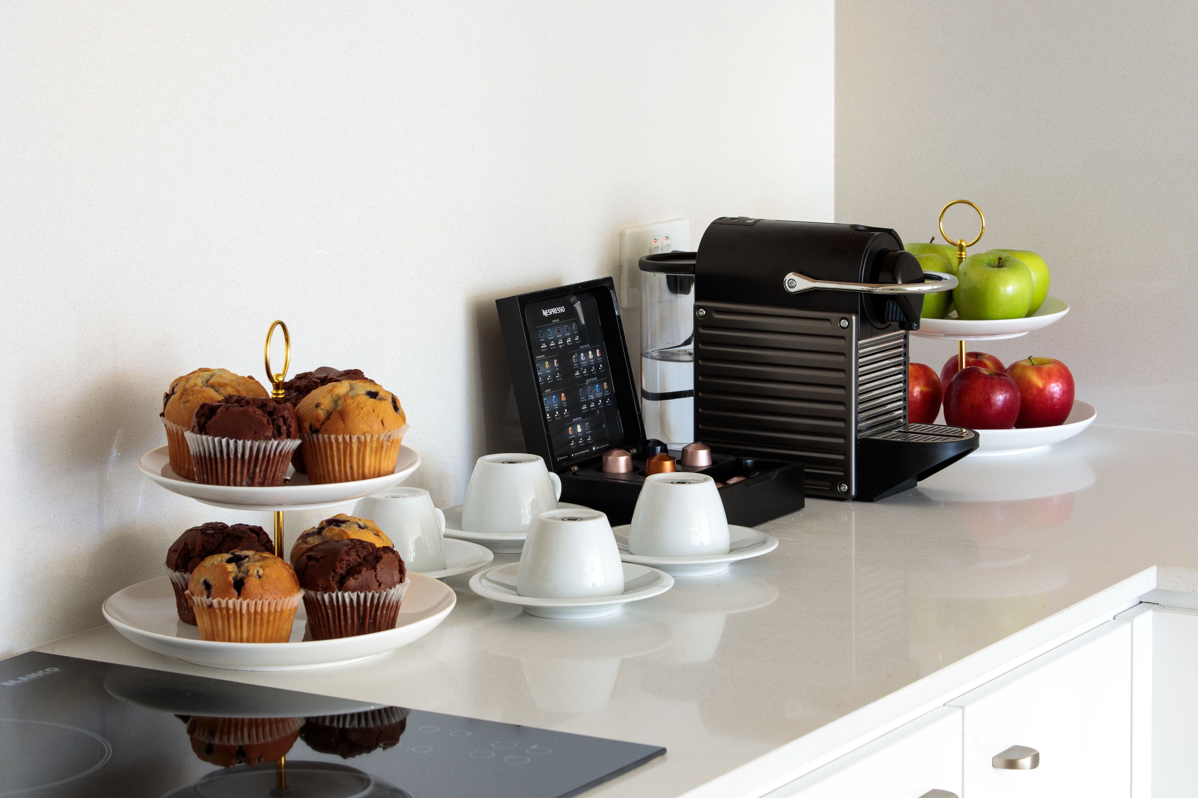 Une table de petit-déjeuner avec des muffins, des tasses de café et des pommes, le tout disposé sur un comptoir.