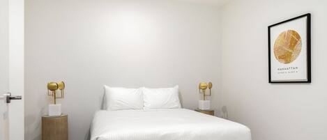 Un dormitorio ordenado con una cama grande, dos mesitas de noche con lámparas y un mapa enmarcado en la pared.
