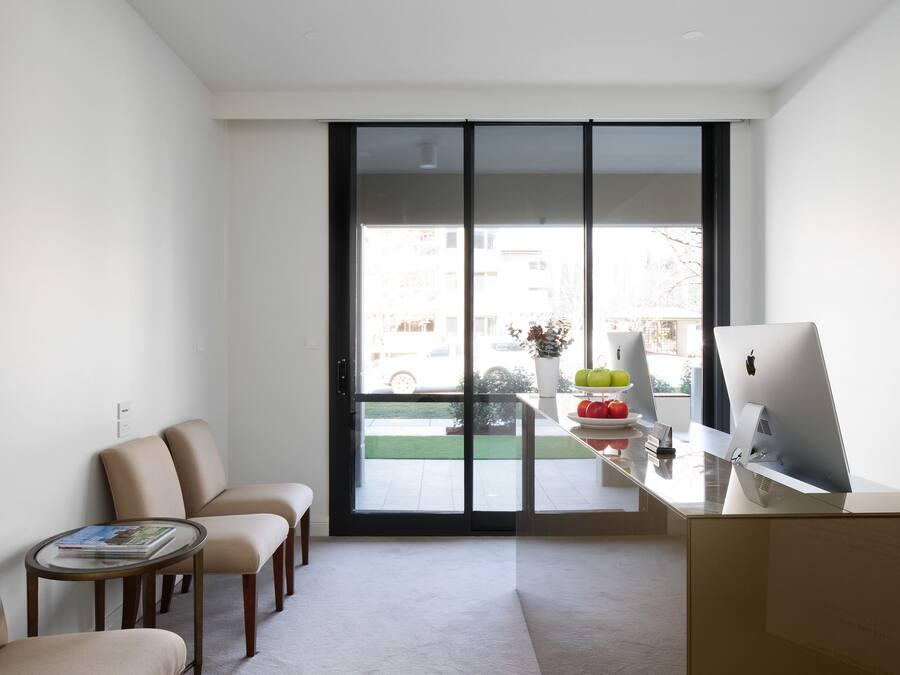 En moderne stue med en stor skydedør til en balkon, et skrivebord med en computer og to komfortable lænestole.