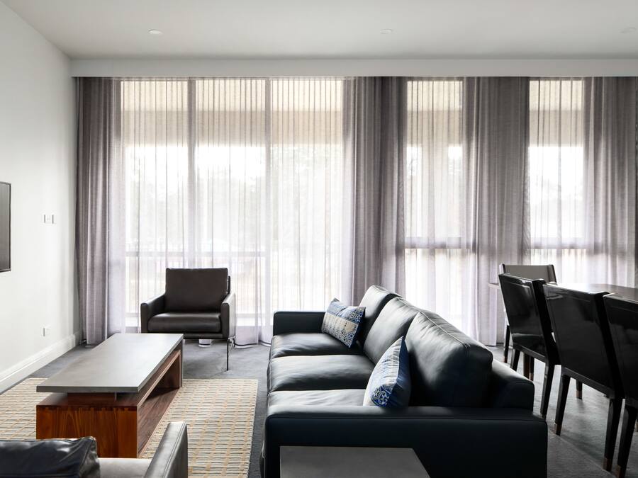 En moderne stue med en lædersofa, et sofabord, et fjernsyn ophængt på væggen og et spiseområde med stole og et bord.