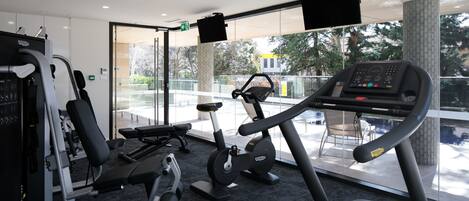 Un gimnasio moderno con equipo cardiovascular, máquinas de pesas y un amplio ventanal con vistas al exterior.