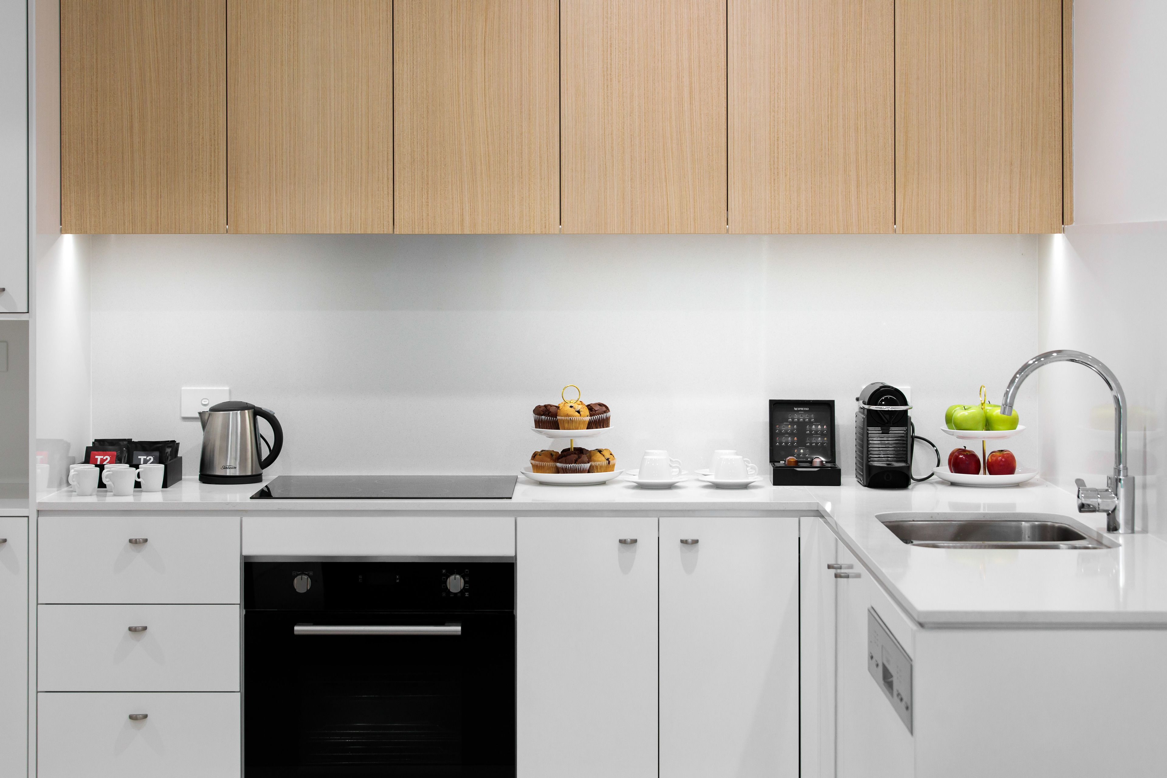 A modern kitchen with white cabinetry, a built-in oven, a coffee maker, and a fruit bowl.