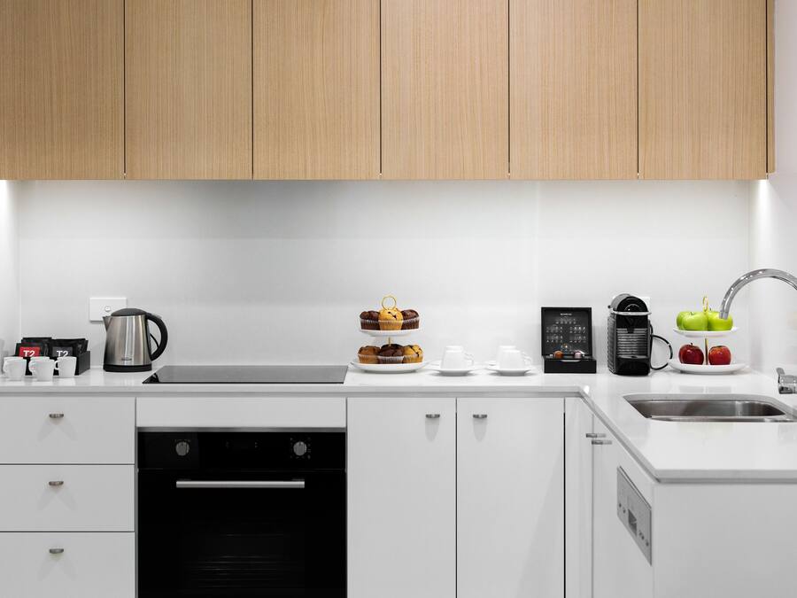 Una cocina moderna con armarios blancos, horno integrado, cafetera y frutero.