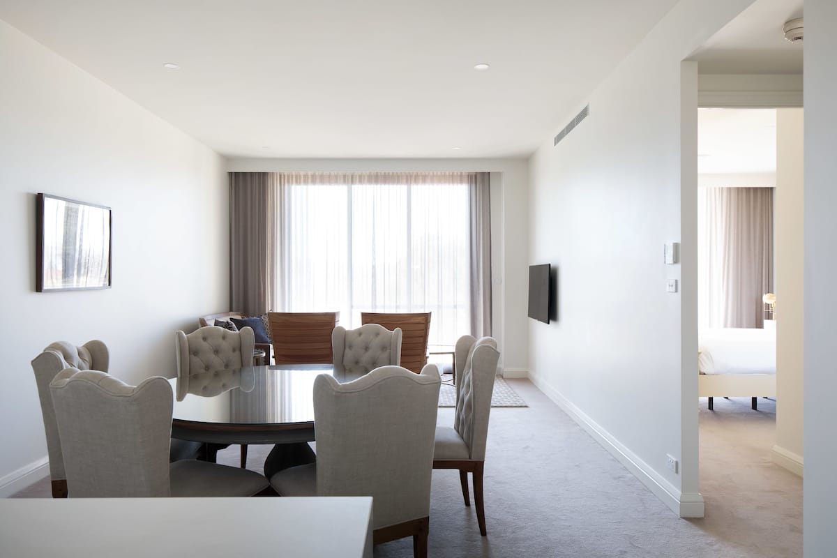 Una habitación de hotel moderna con zona de comedor que incluye una mesa redonda y seis sillas tapizadas.