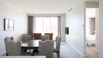 A modern hotel room with a dining area featuring a round table and six upholstered chairs.