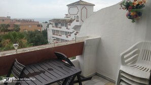 A balcony with a table and chairs, overlooking a cityscape with buildings and a view of the sea.