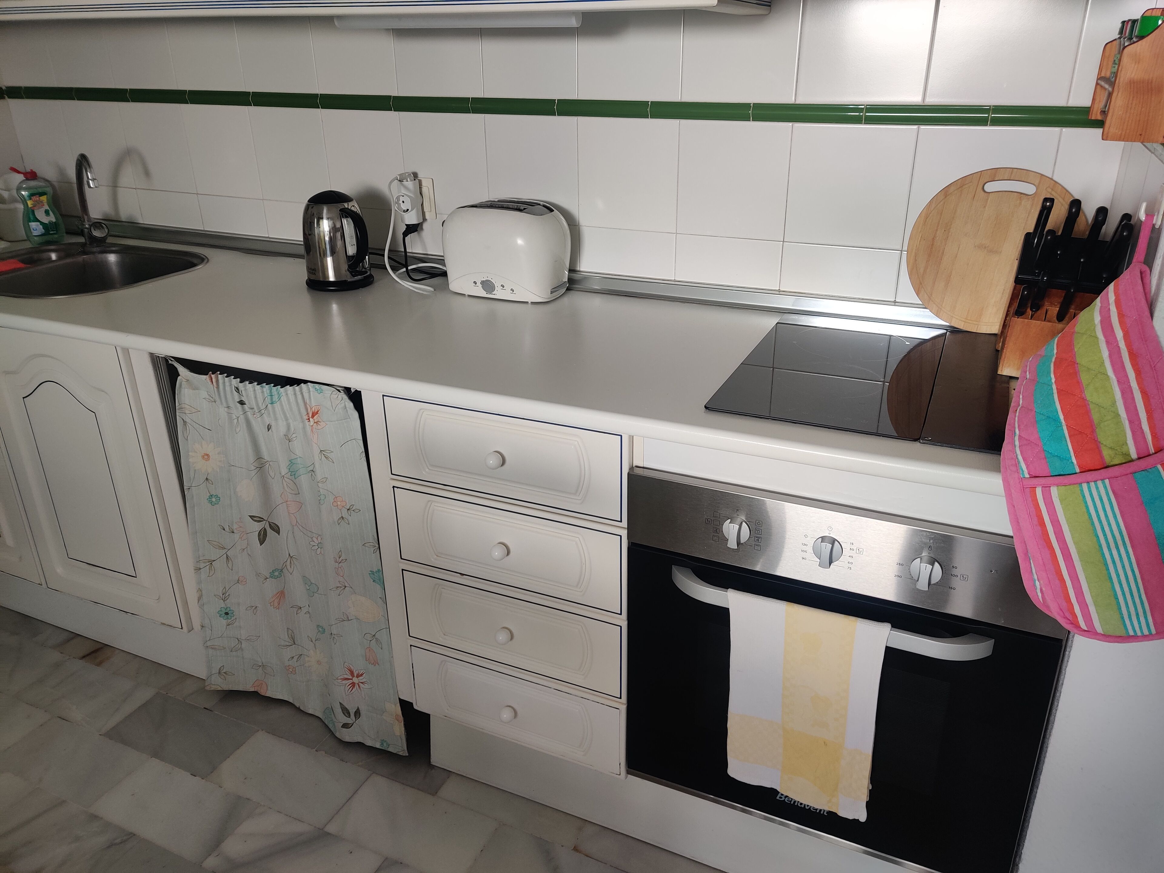 A kitchen with a sink, kettle, toaster, and oven.