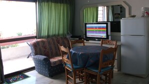 A living room with a sofa, dining table, chairs, a television, and a refrigerator.