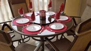 A round dining table with six chairs, each with a red napkin and a glass of water. The table is set with white plates, silverware, and a decorative candle.