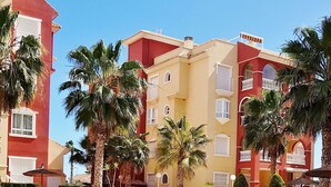 A swimming pool surrounded by palm trees and multi-story buildings with balconies.