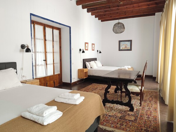 A hotel room with two beds, a dining table, a chair, a patterned rug, and a ceiling light fixture.