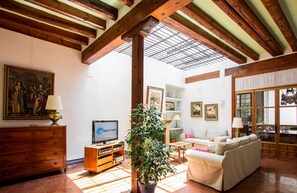 A living room with a TV, wooden furniture, a potted plant, and a painting on the wall.