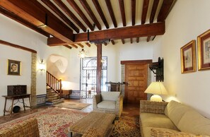 A cozy living room with wicker furniture, a wooden staircase, and a stone wall.