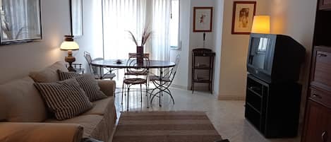 A living room with a sofa, a coffee table, a TV stand, and a dining area with a table and chairs.