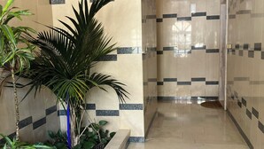 Un couloir aux murs carrelés et au plafond en bois, qui mène à une zone douche.