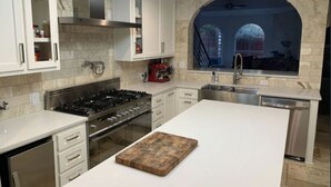 Una cocina moderna con armarios blancos, una isla central, una estufa a gas y vistas a través de un ventanal arqueado.