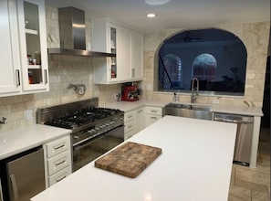 Une cuisine moderne avec des meubles blancs, un îlot central, une cuisinière à gaz et une vue à travers une fenêtre en arc de cercle.