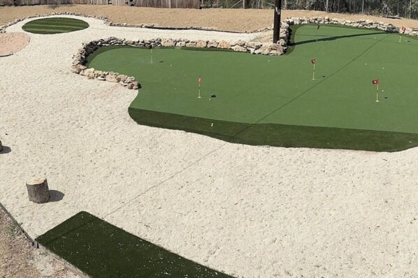 A miniature golf course with sand traps, a green putting area, and a stone border. - Bachelor  Party HQ, pickleball/golf, 16 beds. DT (Austin)