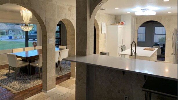 Una cocina moderna con una isla central, paredes de piedra y un arco de entrada a un área de comedor.
