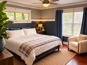 A bedroom with a bed, bedside table, lamp, chair, and a large window with curtains. - Bachelor  Party HQ, pickleball/golf, 16 beds. DT (Austin)