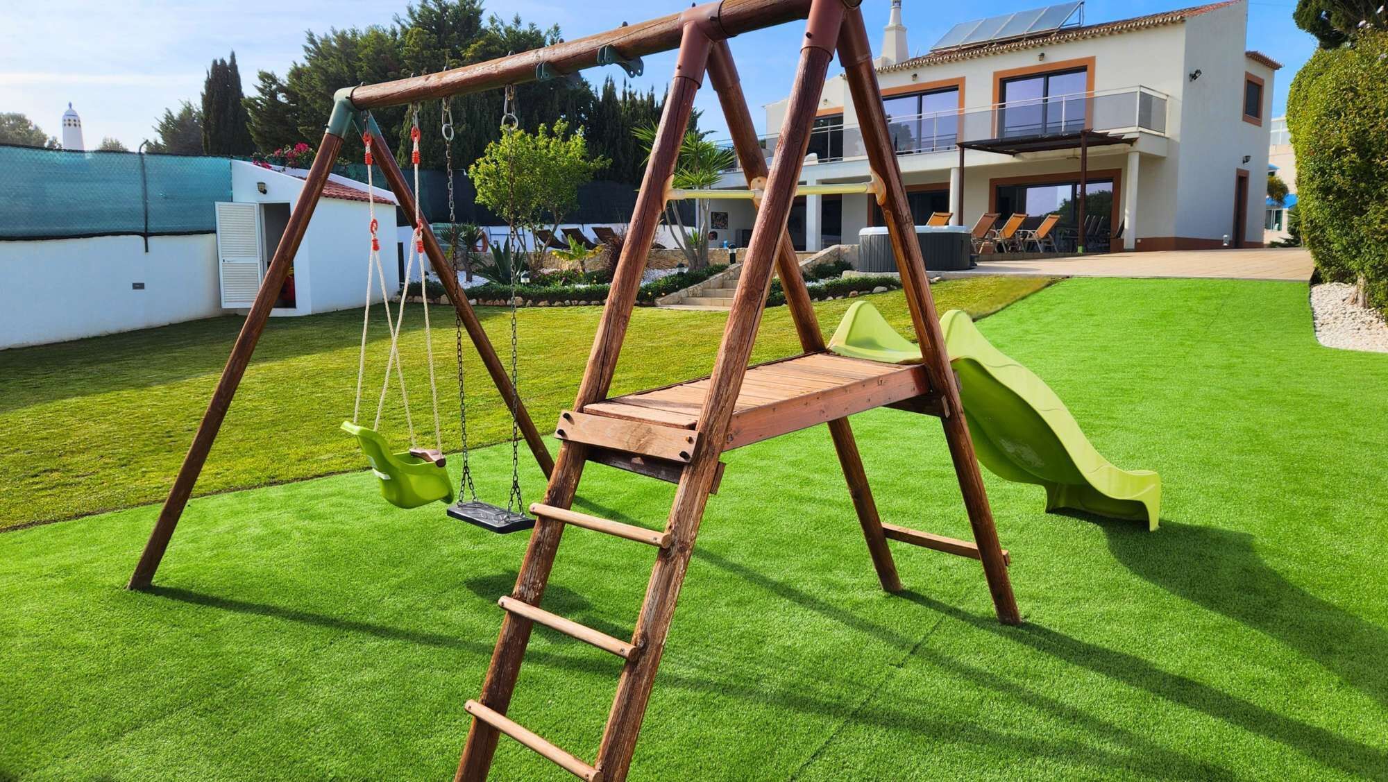 A wooden swing set with a slide in a well-maintained grassy yard.