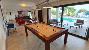 Una mesa de billar en una habitación con vistas a una piscina, un sofá y un comedor.