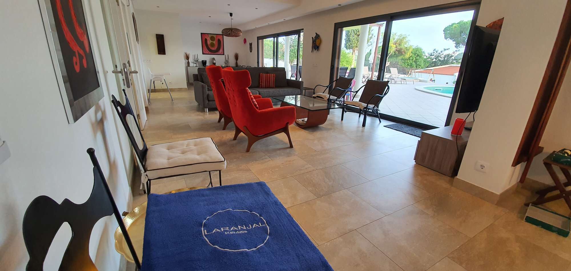 A hotel room with a dining area, a red chair, a blue towel, and a view of the outdoors.